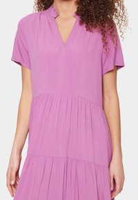 Rosa klänning i mjukt tyg, med v-ringning, korta ärmar och en flerlagers kjoldesign med subtila rynkor.