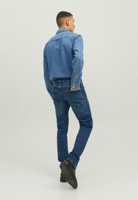 Világoskék farmering hosszú ujjal és gallérral, sötétkék skinny farmernadrággal és fekete cipővel párosítva. Sima textúra és laza stílus.