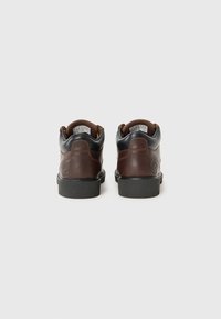 Bruine leren schoenen met een zwarte bovenkant, ronde vorm, gevoerde kraag, rubberen zool en logo in de achterkant geperst.