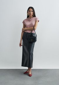 Light pink short-sleeve top, black leather long skirt, red pointed toe heels, and a small black handbag with a gold accent.