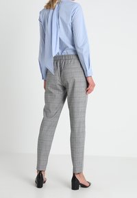 Szare spodnie w kratę z elastycznym pasem, zestawione z jasnoniebieską bluzką z wiązaniem z tyłu i długimi rękawami.