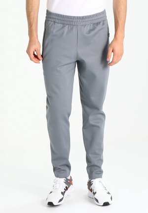 Man wearing gray athletic pants and white sneakers, standing against a white background with hands relaxed at sides.