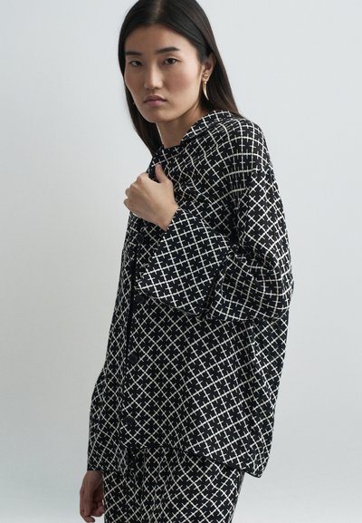 Camisa de botones de patrón en blanco y negro con un diseño geométrico de cruces, que presenta un corte holgado y mangas anchas, confeccionada con una tela suave.