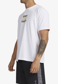 White cotton t-shirt featuring "BRAIN FREEZE" graphic in black and gold, rounded neckline, short sleeves, and a relaxed fit.