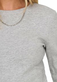 Maglietta grigia a maniche lunghe in un morbido tessuto testurizzato con scollatura a girocollo. Collana in argento a catena sovrapposta.