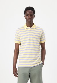 Polo à rayures jaune avec des rayures violettes claires, à manches courtes et col jaune. Présente un logo "GAP" brodé sur la poitrine.