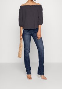 Mörkgrå av-axel topp med volangkrage, trekvartsärmar, matchad med blå raka jeans och klara klacksandaler.