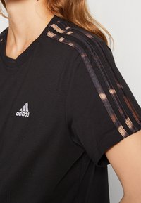 Černé bavlněné tričko s kulatým výstřihem, krátkými rukávy a třemi jemnými hnědými pruhy na ramenou. Logo Adidas na hrudi.