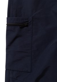 Primissimo piano di una tasca in tessuto blu navy con una zip nera su un indumento, che mostra dettagli di cucitura e texture.