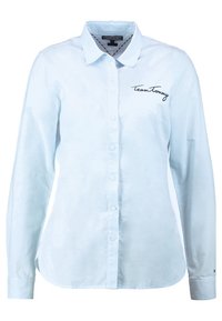 Light blue long-sleeve shirt with button closure, collar, and "Team Tommy" embroidered in black on the chest. Smooth, lightweight fabric.