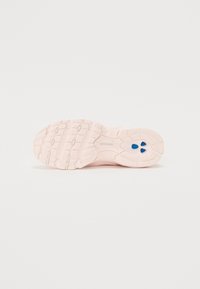 Semelle d'une chaussure de sport rose clair avec un motif de traction texturé et des accents bleus. Présente un design arrondi et rembourré pour le confort.