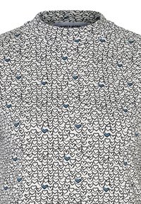 Weißes Oberteil mit hohem Kragen, das mit einem durchgehenden Druck von überlappenden schwarzen und blauen umrandeten Herzen versehen ist. Glatte Textur, leichtes Material.