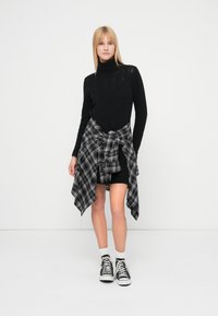 Juodas megztas golfas su tekstūriniu raštu, derinamas su juoda ir pilka languota flaneline palaidine, susirišta mazgu. Juodi šortai ir sportbačiai užbaigia įvaizdį.