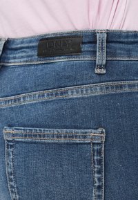 Σκούρα μπλε τζιν τζιν με μαύρη δερμάτινη ετικέτα στη μέση με την ένδειξη "ONLY", διαθέτοντας ορατή ραφή και σχεδιασμό πίσω τσέπης.