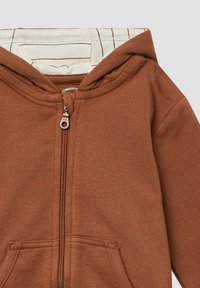 Felpa marrone con zip, dotata di cappuccio con cordino, tasche frontali e una texture morbida. All'interno presenta un rivestimento a righe di colore chiaro.