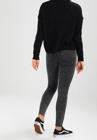 Suéter negro de punto combinado con jeans ajustados grises de talle alto. Conjunto complementado con zapatillas negras con acentos blancos. Tejido texturizado.