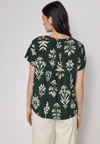 Camicia con motivo floreale in tessuto verde scuro, con stampe botaniche color crema; maniche corte e vestibilità rilassata, con un piego sul retro.