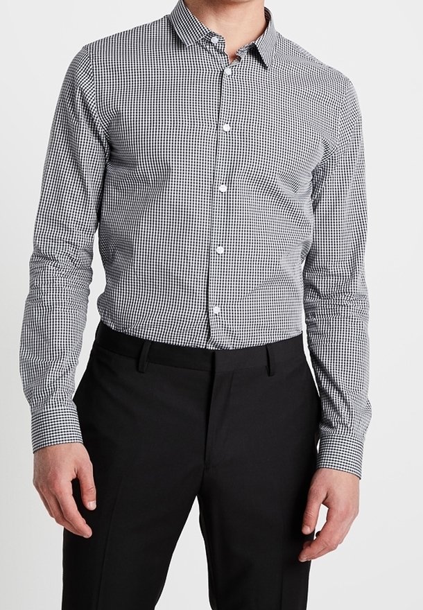 Chemise à carreaux noir et blanc avec un col écarté, des manches longues et une coupe ajustée, associée à un pantalon noir.