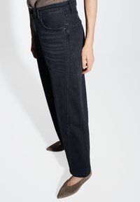 Pantalons en denim bleu foncé avec une coupe décontractée, dotés de poches avant et arrière, et d'une texture lisse. Portés avec des ballerines pointues marron clair.