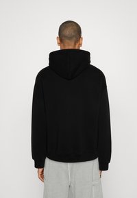Sweat à capuche noir avec une coupe décontractée, une texture douce et des poignets côtelés. Le dos présente un design épuré et simple.