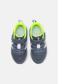 Baskets de sport grises avec une tige en maille, accents blancs et doublure vert fluo. Comprend une sangle Velcro et des lacets pour un ajustement sécurisé.