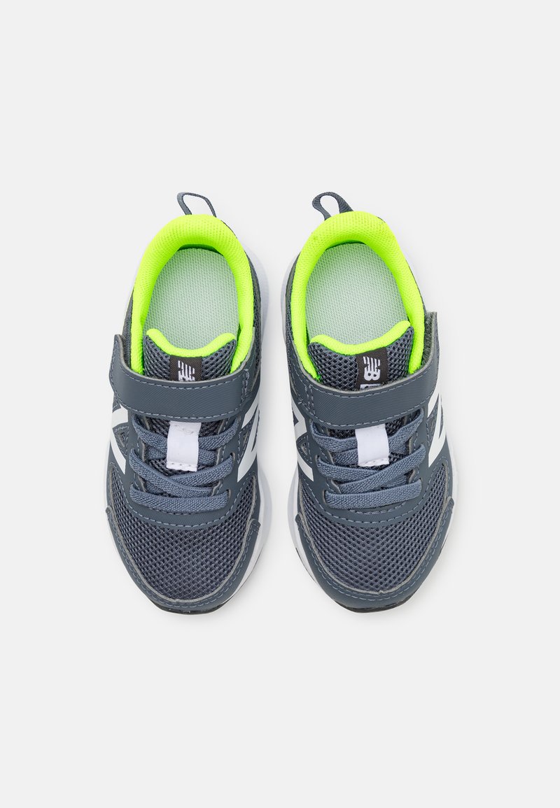 Baskets de sport grises avec une tige en maille, accents blancs et doublure vert fluo. Comprend une sangle Velcro et des lacets pour un ajustement sécurisé.