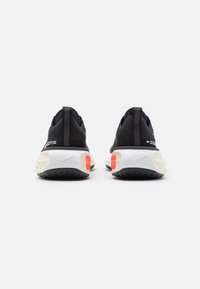 Sneakers atletici neri con una tomaia texturizzata, intersuola bianca, dettagli arancioni e suola in gomma nera. La vista posteriore rivela dettagli del marchio.