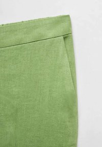 Groene linnen stof met een gladde textuur. Heeft een keurig gevouwen tailleband en een diagonale zijzak.