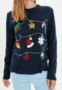Dunkelblauer Pullover mit bunten, glitzernden Weihnachtsornamenten, darunter Hüte, Sterne und Schneeflocken, umrandet von weißem Stickerei.