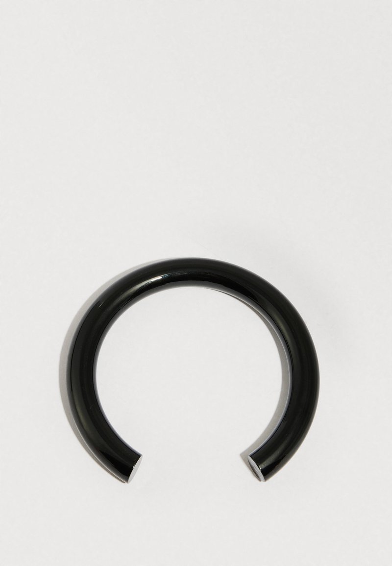 Musta kiiltävästä materiaalista valmistettu pyöreä rannekoru, jossa on sileä pinta ja avoin muoto neliönmuotoisine päineen.