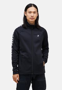 Sort zip-up jakke lavet af glat stof, med høj krave, sidelommer og hvide logo- og tekstdetaljer på ærmerne.