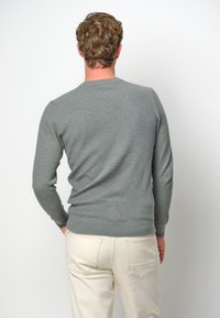 Grå stickad tröja med långa ärmar och rund halsringning, i kombination med ljusbeige byxor. Strukturerad tyg och figurnära design.