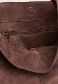 Brun ruskinds bag indvendig, som viser en lynlås lomme og magnetlukning på et blødt tekstureret stoffor.