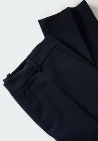 Paire de pantalons noirs sur mesure, pliés, avec passants de ceinture et poches latérales sur fond blanc.