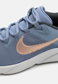 Chaussure de sport bleue avec une texture côtelée, un logo Nike en rose doré et des accents gris, dotée d'une semelle rembourrée et d'un design de lacets tissés.