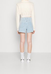 Ljust blå denimshorts med hög midja och bakfickor, tillsammans med en kort creamfärgad tröja och vita strumpor med svarta detaljer.