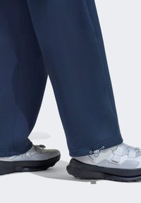 Laivastonsiniset urheiluhousut, joissa on sileä pinta, yhdistetty harmaisiin ja valkoisiin lenkkareihin, joissa on kestävä pohja ja säädettävät nauhat.