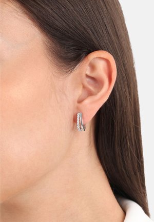 Pendientes de aro de plata con un diseño retorcido que presenta pequeñas piedras transparentes a lo largo de un lado, brillando contra un acabado metálico suave.