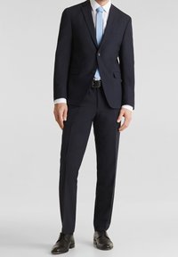 Completo blu navy con una vestibilità su misura, revers a bastone, bottone singolo e tasca; cravatta azzurra chiara; scarpe eleganti in pelle nera; camicia con colletto bianco.