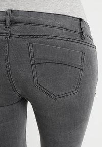 Jeans de mezclilla gris con un diseño ajustado, costuras visibles y un bolsillo trasero con un sutil borde curvado. Textura suave.