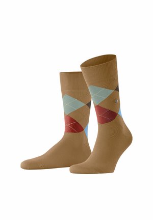 Para brązowych skarpetek z wzorem argyle z niebieskimi, czerwonymi i zielonymi rombami na białym tle.