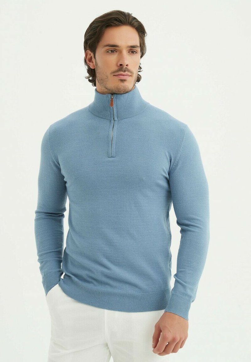 Pull en maille turquoise avec col zippé, à manches longues et poignets côtelés. Doté d'une courte fermeture éclair avec une tirette en cuir.