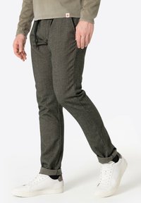 Dunkelgraue, strukturierte, tapered Hosen mit einem Kordelzugbund. Getragen mit weißen Turnschuhen mit grauen Akzenten und hochgekrempelten Säumen.