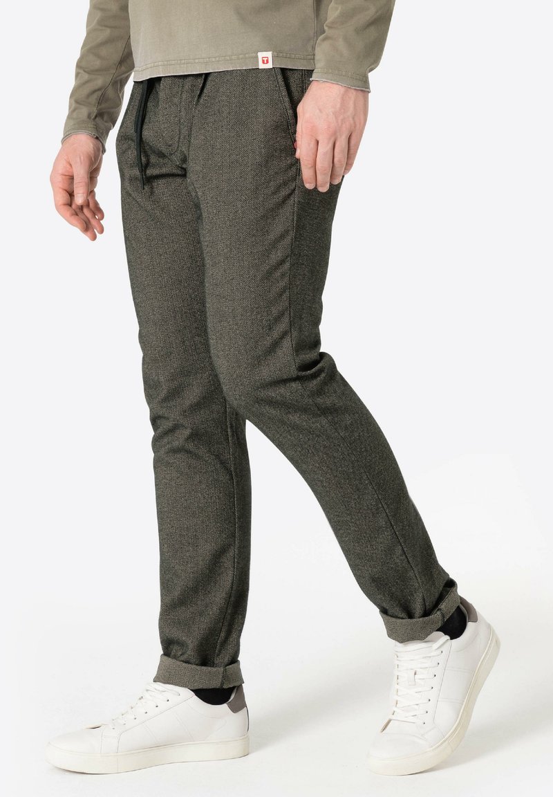 Dunkelgraue, strukturierte, tapered Hosen mit einem Kordelzugbund. Getragen mit weißen Turnschuhen mit grauen Akzenten und hochgekrempelten Säumen.