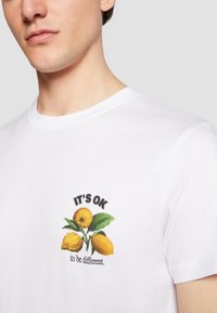 Fehér pamut póló, színes citrom grafikával és a "JÓ, HA KÜLÖNBÖZŐ VAGY" felirattal. Rövid ujjú, kerek nyakú.