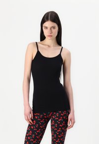 Svart ärmlös topp med tunna axelband, slät textur, i kombination med svarta leggings med ett röd körsbärsmönster på en mörk bakgrund.