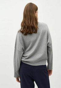 Maglione grigio a maglia con una vestibilità rilassata, spalle scese e maniche lunghe, abbinato a pantaloni blu navy. La texture sembra morbida e leggera.
