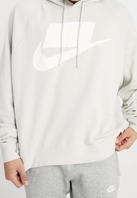Ljusgrå Nike hoodie med en stor vit logga. Har en dragsko för huvan, långa ärmar och ribbade ärmslut och nederkant. Mjuk textur.
