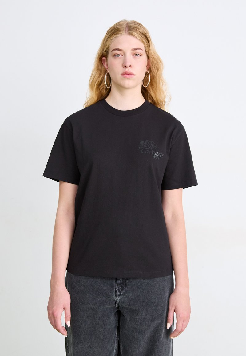 Czarny bawełniany t-shirt z krótkimi rękawami i okrągłym dekoltem, z delikatnym szarym wzorem graficznym na klatce piersiowej. Noszony z ciemnoszarymi spodniami.