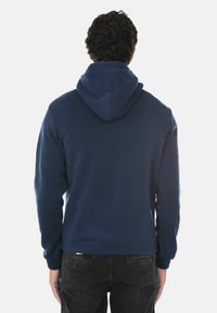 Felpa blu navy realizzata in misto cotone, dotata di tasca a marsupio, polsini a coste e cappuccio con cordino. Il retro è semplice, senza loghi visibili.